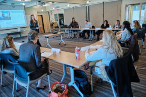 Photo of Together in Recovery meeting attendees sitting at tables around a large room with the facilitator in the middle